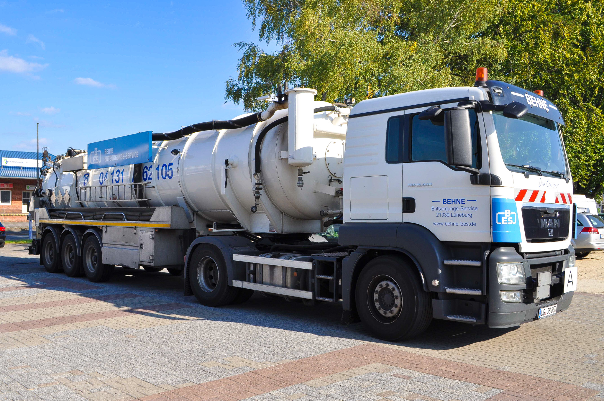 Sattelzug der Behne Entsorgungs-Service GmbH, MAN TGS Zugmaschine mit Vakuumtank-Auflieger, silberner Edelstahltank mit blauer Firmenbeschriftung, geparkt auf gepflastertem Betriebsgelände in Lüneburg